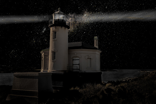 A Lighthouse shines through the night under a starry black sky. Color image.