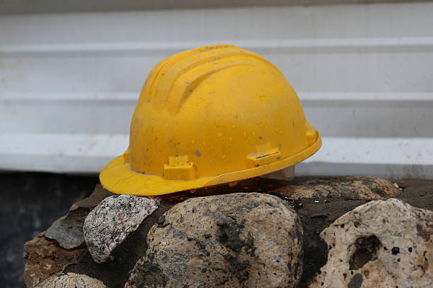 Work Helmet Work helmet of a construction worker on a rock fence in the construction site. Wet safety helmet of a construction worker in front of a corrugated iron fence in a rainy day. corrugated metal fence ideas stock pictures, royalty-free photos & images