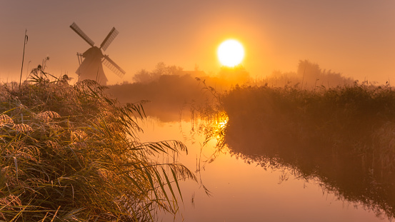 Typical historic windmill in a polder wetland on a cool colored foggy september morning in the Netherlands