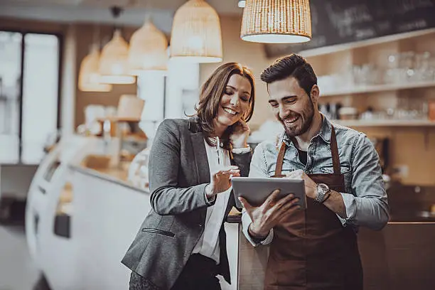 Shot of a smiling cafe owner  and employee barista standing inside a coffee shop looking at new menu on a digital tablet