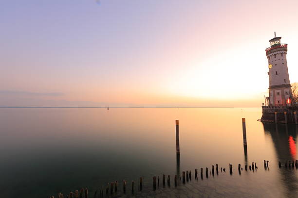 Long exposure shot looking at Lake Constance at Lindau with its lighthouse during blue hour that shows a beautiful, calm, colorful and peaceful landscape. Optical distortion from ultra wide lens make the lighthouse st the right border of the image look tilted.