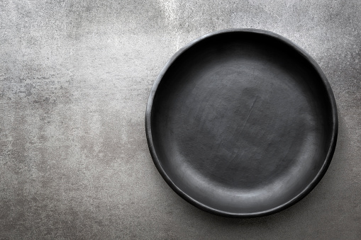 Empty rustic black plate over gray slate.  Aerial view, with copy space.