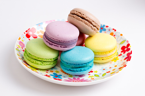 Collection of brightly colored French macarons on white background, lying in a saucer
