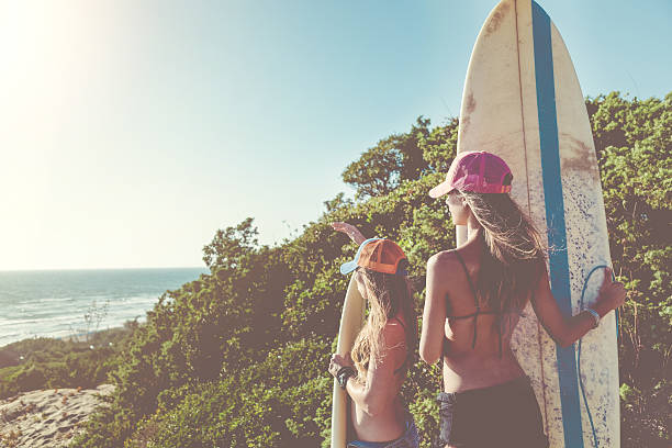 Surfer girls going to the sea Surfer girls standing at the sea with surfboards, during a warm sunny summer day surfboard fin stock pictures, royalty-free photos & images