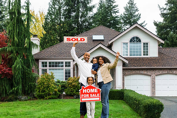 Enthusiastic Family with Home For Sale Portrait of a young family standing in front of house, holding a Home For Sale sign with arms raised enthusiastically. selling stock pictures, royalty-free photos & images