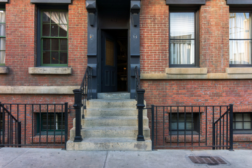 A brownstone stoop, sidewalk, stairs with an open door.