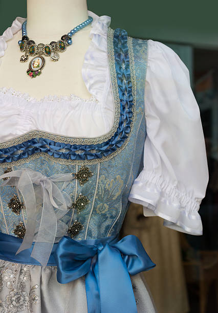 Detail Blue Dirndl dress  with  classic bodice, necklace and blue silk bow. over a white ruffled lace blouse worn by a fashion mannequin 