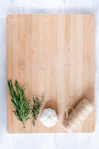 fresh herbs, garlic and twine roll on bamboo chopping board from overhead, cooking background