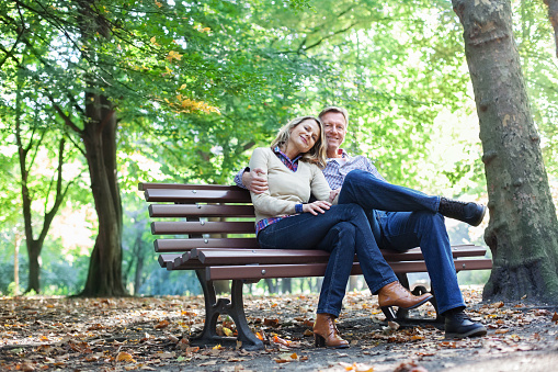Portrait of affectionate mature couple sitting on a bench in park during autumn
