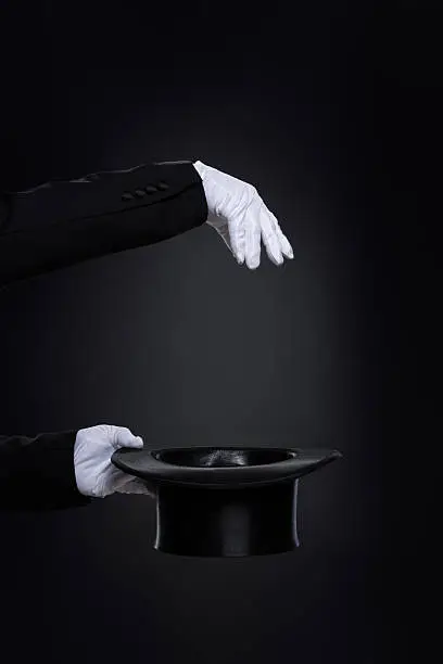 MagicianËs hands in white gloves with top hat over black