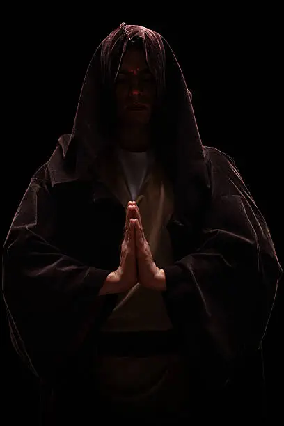 Vertical shot of a monk with a hood on his head praying on black background