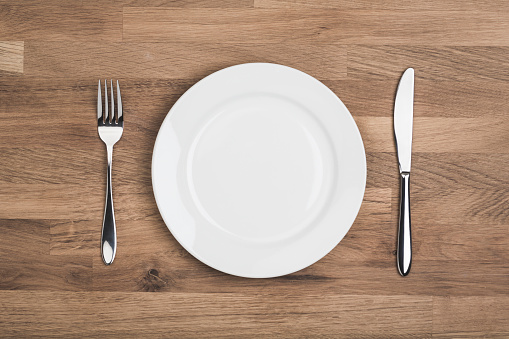 Empty white plate with knife and fork, Overhead shot on wooden table