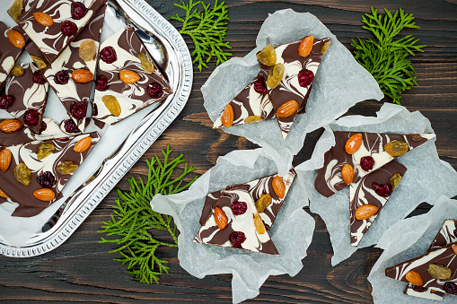 Holiday chocolate bark with dried fruits and nuts on a dark wood background. Top view. Dessert recipe for judaic holiday Tu Bishvat