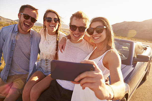 istock Friends On Road Trip Sit On Convertible Car Taking Selfie 503545758