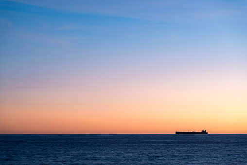 Silhouette  of cargo ship on the horizon viewed from bay with rock