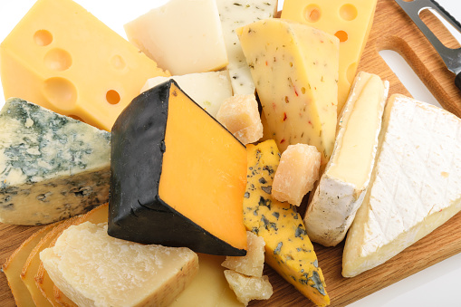 Cheese platter on a wooden cheese board with grapes, biscuits, jam and cheese knife in the photograph. There are also some cheese biscuits in the background.