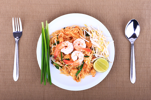 Fried noodle Thai style with prawns, Stir fry noodles with shrimp in padthai style on table. Front view isolate white , brown background