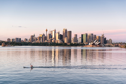 Sydney, Australia - November 18, 2015: A kayaker is passing by while the sunset is on the Sydney skyline. Central Business District and the Opera House is in the background. 