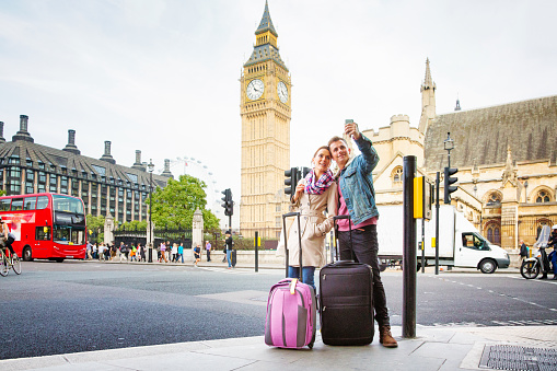 Young tourist couple shoots selfie in front of Big Ben in London, UK. Their luggage stands in front of them.