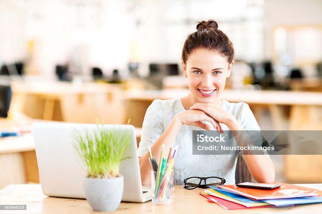 Smiling Entrepreneur Sitting At Desk Portrait of smiling female entrepreneur sitting at desk in office. Horizontal shot. Desk Stock Photo