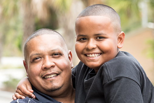 Smiling Hispanic father and son looking at the camera embracing