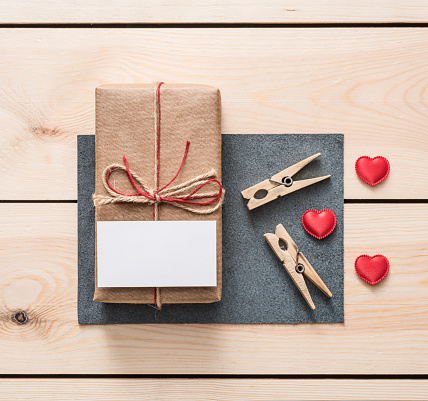 Gift box with white blank tag and hearts on wood. Top view.