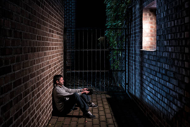 hombre sentado en la noche a continuación solo fuera de la ventana - brick wall homelessness wall begging fotografías e imágenes de stock