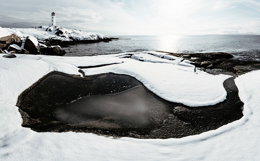 The surrounding landscape at Peggy's Cove Lighthouse is covered with a blanket of fresh snow bathed in late afternoon sunlight.  Stitched panoramic view.