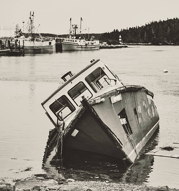Fisherman's Past An abandoned fishing boat in the foreground of a Nova Scotian fishing village wharf.  Toned black and white. fishing village photos stock pictures, royalty-free photos & images
