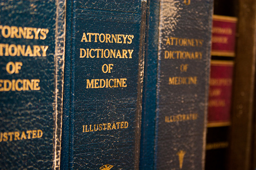 Law books on a bookshelf. Close-up of Attorneys' Dictionary of Medicine title. Worn, blue bindings with gold lettering.