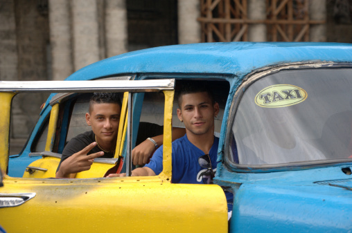 Havana, Cuba - May 20, 2012: Friendly and handsome Cuban young men sitting in a Cuban taxi smile and give the peace or victory hand sign
