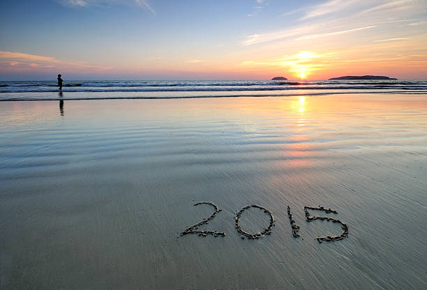 Silhouette of a person and Year 2015 written on sand at Sunset