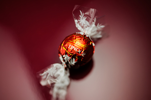 Kilchberg, Germany - March 20, 2014: Lindt Lindor chocolate truffle on a red luxury silk background as seen on March 20, 2014. Lind is one one of the lastgest luxury chocolate and confectionery company worldwide