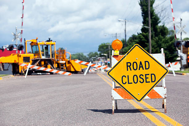 Road Closed for Railroad Crossing Construction A road closed sign at a railroad crossing construction site. In the background is a Ballast (rock) regulator and compactor machine working on a new section of railroad track. This specialized equipment sculpts ballast around rail and ties with a brush, plow and side wings road closed sign horizontal road nobody stock pictures, royalty-free photos & images