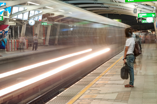 Bangkok, Thailand - December 5, 2010: Long exposure photograph of an elevated train pulling up to a station platform with blurred motion people waiting to board. The Skytrain or Bangkok Mass Transit System (BTS) spans the centre of the Thai capital city.