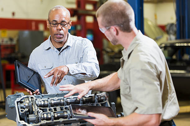 dwie wielofunkcyjne-rasę mechanika z cyfrowy tabletki, mówi - trainee auto repair shop computer manual worker zdjęcia i obrazy z banku zdjęć