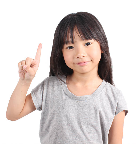 маленькая девочка с ее палец, указывающий на что-то, - little girls pre adolescent child standing isolated стоковые фото и изображения