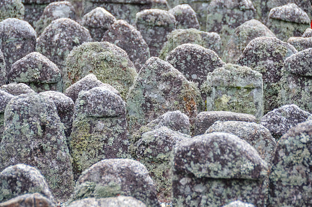 Kyoto, Japan - November 26, 2015: Ancient weathered stone statuettes at Adashino Nenbutsu-ji,  a Buddhist temple in Kyoto, Japan. Situated high on a hill overlooking the city from the northwest, it sits in an area where since the Heian period people abandoned the bodies of the dead, exposing them to the wind and rain. Now, some eight thousand Buddhist statuettes, which had been scattered around Adashino then collected about 1903, memorialize the souls of the dead. During its well-known 'sento kuyo', a ceremony dedicated to the spirits of the dead, about ten thousand stone statues are lit up with candles.