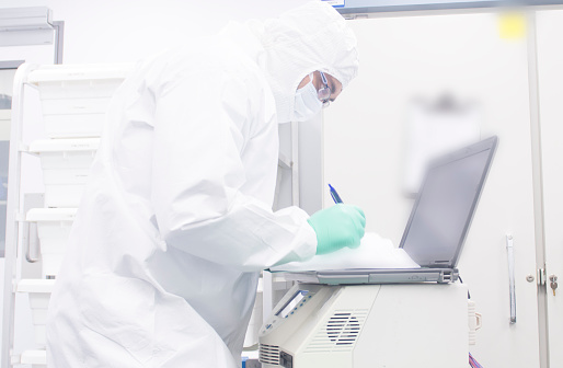 Pharmaceutical scientist working in an aspeptic or sterile or clean room fully gowned and performing qualification of equipment.