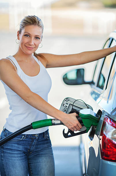 Woman refueling her car at gas station. Closeup of early 30's attractive woman refueling her car at a gas station. She's smiling and looking at camera. Wearing white sleeveless top and jeans. hose photos stock pictures, royalty-free photos & images