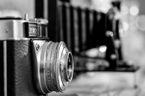 A vintage camera in black and white with slight film grain and a defocussed antique bellows camera in the background with copy space to the top and right.