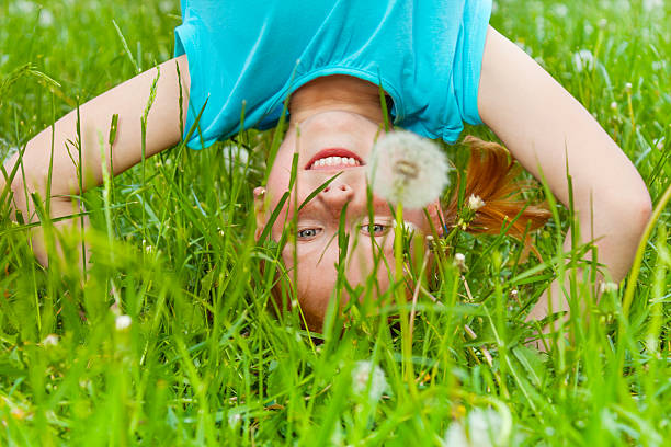 Little smiling girl standing on her head on the grassy meadow