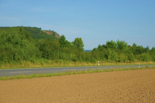 Image of an empty running through farmland and forests with Erpeler Ley in Germany in the distance