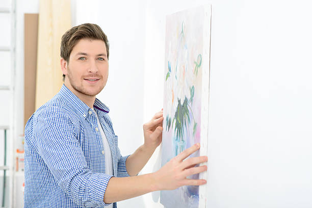 Love art. Close up of happy handsome man holding picture and hanging it on the wall while expressing positivity