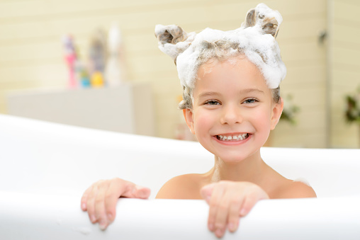 Play with me. Content cheerful little girl sitting in the bath tube and smiling while having fun