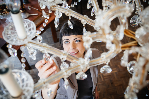 Mature adult woman shopping in an old antique store and touching a chandelier hanging from the ceiling. Shot from an overhead position focusing the woman's face.