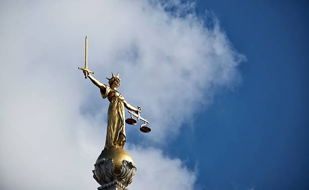 The Old Bailey's Lady Justice Statue Low angle view of the grand, imposing bronze statue of Lady Justice, sitting atop a dome on London's Central Criminal Court, which is more popularly known as the Old Bailey. Bathed in Springtime sunshine, she grasps in her right hand a sword, whilst in her left she holds the scales of Justice.  royal courts of justice stock pictures, royalty-free photos & images