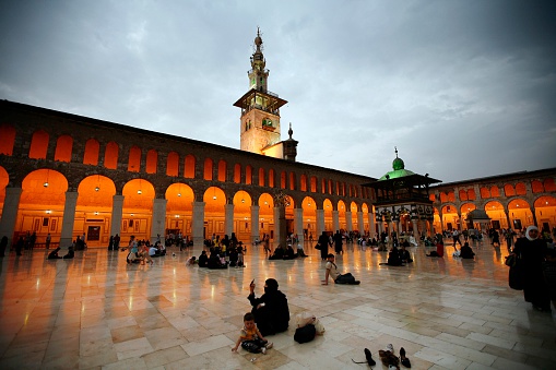 Damascus,Syria -  August 03,2010 : Umayyad Mosque (Grand Mosque of Damascus) - south-western part of courtyard with the Dome of the Treasury (Qubbat al-Khazna, octagonal structure decorated with mosaics)People who pray in the Umayyad Mosque.