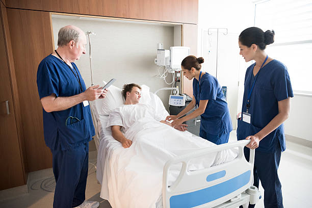 Medical team treating male patient in hospital bed Nurses and doctor on hospital ward with young man. Medical professionals assisting young man in hospital. night table stock pictures, royalty-free photos & images
