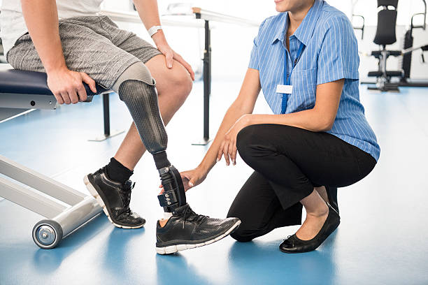 Medical professional helping man with prosthetic leg Male amputee with prosthesis in hospital. Man sitting on chair with nurse touching prosthetic limb. Female nurse working with male patient. Rehabilitation, recovery, improvement. prosthetic equipment photos stock pictures, royalty-free photos & images